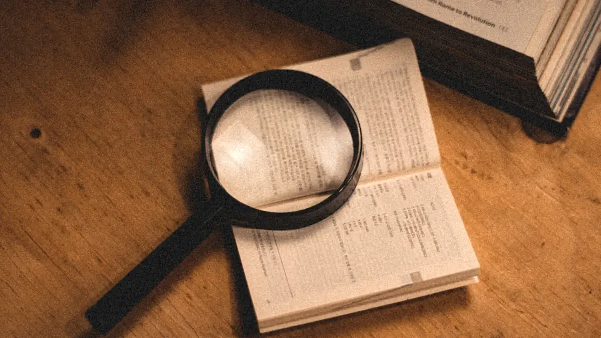 Magnifying glass resting on an open book, revealing what is hidden in the text